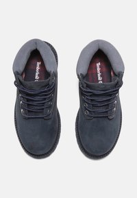 Stivaletti alla caviglia in suede blu scuro con colletto imbottito grigio e lacci blu navy, dotati di una fodera a scacchi e occhielli rinforzati.