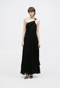 Fekete pliszírozott maxi ruha aszimmetrikus, egyrészes vállmegoldással és finom virágos díszítéssel a vállnál. Simam folyós anyag.