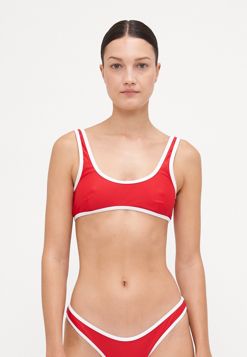 Červený bikiny set pozostávajúci z braletky s výstrihom v tvare lodičky a bielym lemovaním, tenkými ramienkami, v kombinácii s nohavičkami s nízkym pásom a hladkou textúrou.
