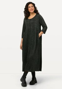 Robe noire scintillante avec un décolleté arrondi, des manches trois-quarts et des poches latérales. Design long et fluide, associée à des bottes noires épaisses.