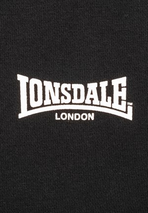 Tela negra con el texto blanco "LONSDALE LONDON". Las letras presentan un diseño audaz y curvado, sobre un fondo texturizado.
