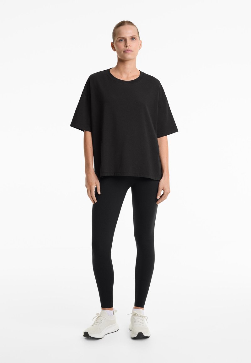 T-shirt noir oversize à manches courtes, associé à des leggings noirs et des baskets blanches. Design simple, texture douce, coupe décontractée.