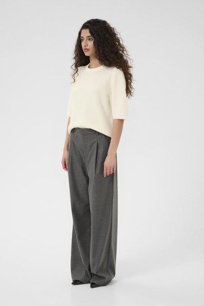 Un pull à manches courtes de couleur crème en matière douce, associé à un pantalon large en gris cintré, avec des plis et des escarpins noirs à bout pointu.