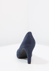 Zapato de tacón alto de color azul oscuro, hecho de un tejido texturizado, con punta afilada y tacón estilizado, y una suela negra lisa.