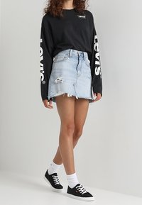 Camisa negra de manga larga con el logo blanco de "Levi's", falda de mezclilla azul claro con dobladillo deshilachado y desgaste, zapatillas negras, calcetines blancos.