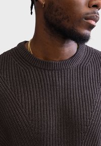 Strikket mørkebrun sweater med ribstruktur og rund halsudskæring, der har et subtilt mønster, som fremhæver skuldrene.