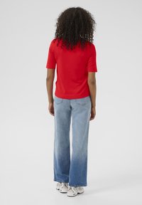 Rode top met korte mouwen gecombineerd met lichtblauwe wijde jeans. De jeans hebben een geleidelijk kleurverloop. Sneakers zijn beige met textuurdetails.
