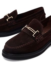 Mocassins en daim brun foncé avec semelles noires et détailles d'une boucle en métal doré sur le dessus avant.