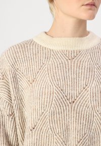 Gestrickter Pullover in Beige mit einem cremefarbenen, gerippten Kragen. Verfügt über ein strukturiertes Muster mit wellenförmigen Linien. Weicher, leichter Stoff.