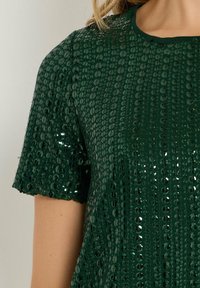 Top verde a maniche corte adornato con paillettes lucide, con scollatura rotonda. Il tessuto ha una finitura testurizzata e scintillante.