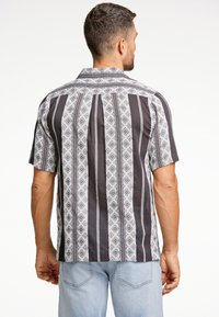 Camisa de manga corta en tela de algodón negro y blanco, con rayas verticales y patrones geométricos, con un collar clásico y dobladillo recto.