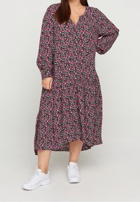 Robe à imprimé floral avec des manches longues, décolleté en V, ourlet à volants et fond noir. Portée avec des baskets blanches. Le tissu est léger et fluide.