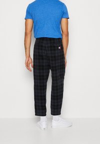 Czarne spodni w kratę o luźnym kroju, z małą naszywką z logo, w połączeniu z białymi sneakersami i niebieską koszulką.