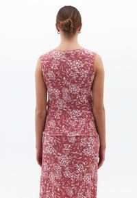 Vestido sin mangas con un estampado floral en tonos rojos y blancos, fabricado en un tejido texturizado, con un diseño ajustado y un ligero peplum en la cintura.