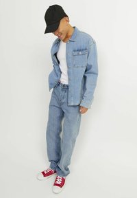 Jachetă din denim de culoare albastru deschis, cu două buzunare pe piept și blugi largi asortați, completată cu adidași roșii și o șapcă neagră.