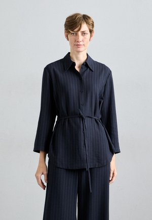 Navy blue pinstriped blouse with long sleeves, a collar, and a tie waist detail. Made of soft fabric with a smooth texture.