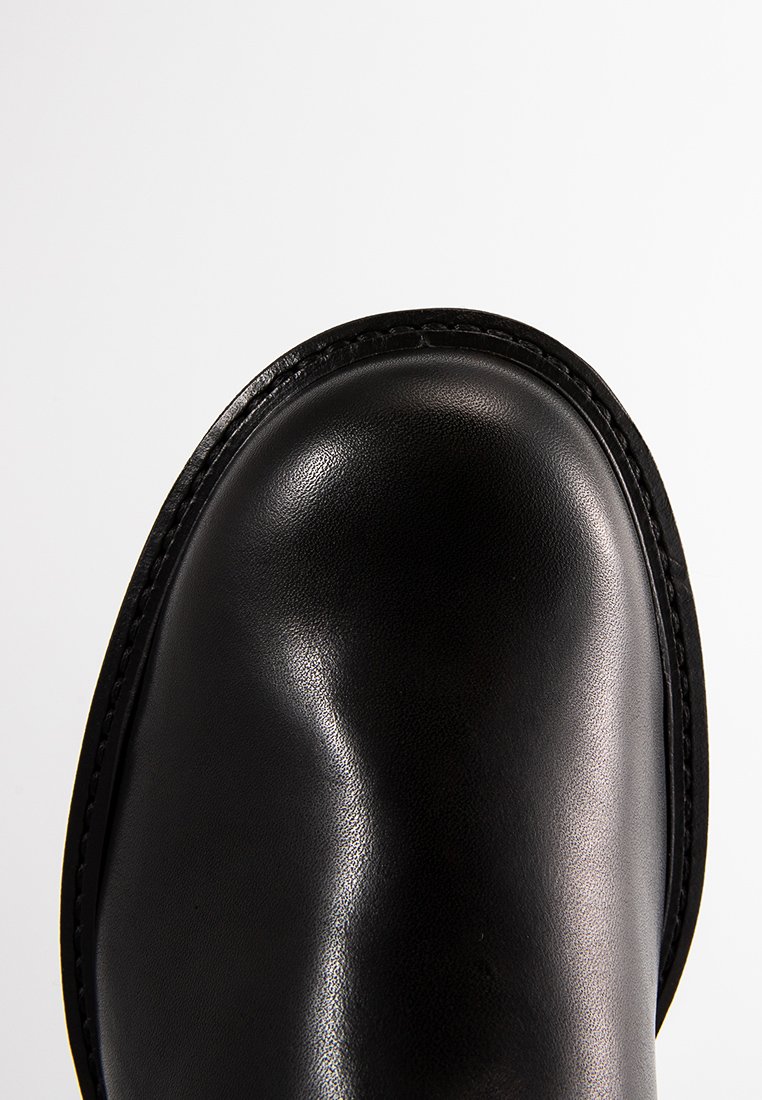 Schwarzer Lederschuh mit runder Zehenform, glatter Textur und sichtbaren Nähten entlang der Kante. Leichtbauweise, minimalistisches Design.