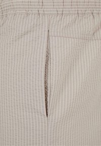 Tissu texturé beige avec de fines rayures verticales, présentant une couture ouverte et une taille élastique, mettant en avant des détails de conception simples et fonctionnels.