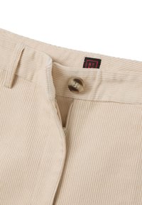 Beige Corduroyhosen mit vertikalen Rippungen, ausgestattet mit einem Reißverschluss und einem runden, gemusterten Knopf. Das Etikett zeigt "ST" in schwarz auf rotem Hintergrund.