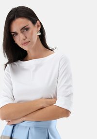 Weißes, langärmliges Oberteil mit Rundhalsausschnitt, kombiniert mit einem hellblauen, plissierten Rock. Der Stoff wirkt glatt und weich, mit einer figurbetonten Silhouette.