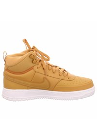 Baskets montantes Nike en jaune moutarde, avec une tige en cuir lisse, des accents texturés, des lacets plats et une semelle en caoutchouc blanc.