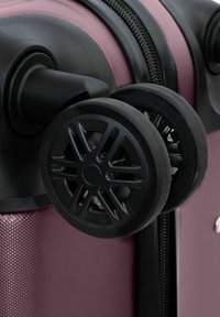 Gros plan sur des roulettes noires doubles attachées à une valise rigide violette texturée, près de la fermeture éclair.