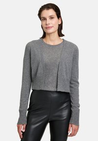 Cardigan court gris, texture côtelée, ouverture à l'avant, manches longues. Porté par-dessus un haut ajusté gris et associé à un pantalon en cuir noir.