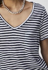 Person wearing a black and white striped V-neck shirt with a small chest pocket and a thick silver chain necklace.