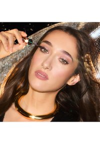 Schwarzes Paillettenoberteil, goldene metallische Kragenkette, Mascara auftragen. Lange dunkle Haare, akzentuierte grüne Augen, sanfte pinke Lippen, schimmernder Hintergrund.