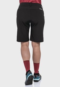Schwarze Shorts mit glatter Textur, ausgestattet mit einem breiten Bund und umgeschlagenen Säumen. Kombiniert mit roten Socken und Schuhen mit blauen Akzenten.