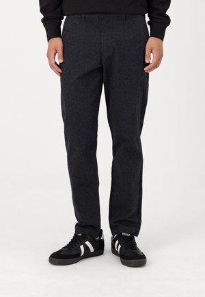 Dunkelgraue, strukturierte Hose mit geradem Schnitt, Gürtelschlaufen und Fronttaschen, kombiniert mit schwarzen Sneakers mit weißen Streifen.