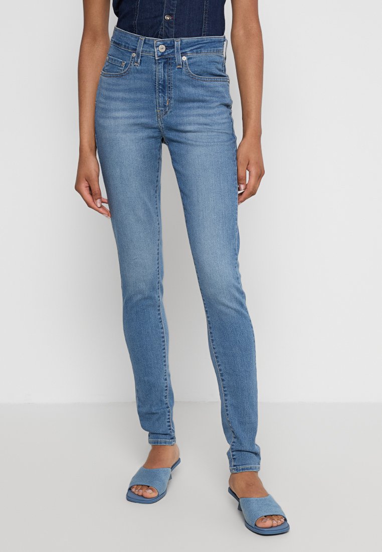 Jeans slim taille haute de couleur bleue claire en denim, avec un design à cinq poches et des décolorations subtiles. Associés à des sandales à glissière bleues assorties.