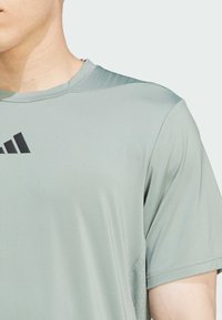 Lys grøn atletisk T-shirt lavet af fugtabsorberende stof, med rund halsudskæring og sort logo detalje på brystet.