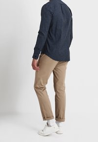 Camisa azul marino de manga larga con pliegue en la parte posterior, combinada con pantalones beige entallados con los puños remangados y zapatillas blancas con suelas texturizadas.