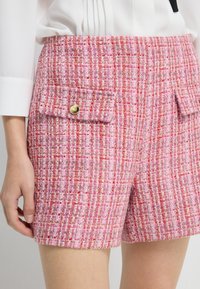 Růžové tweedové šortky s texturovaným tkaním, vybavené dvěma předními kapsami s klopami a zlatými detaily na knoflících, navržené s vysokým pasem.