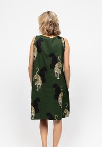 Donna bionda di spalle che indossa un vestito senza maniche di colore verde scuro con un motivo a stampa leopardata nero e giallo.