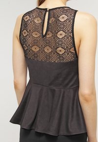 Top peplum negro con espalda de encaje y patrones geométricos, tejido suave y detalle de escote en forma de llave.