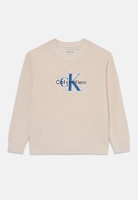 Beige kötött pulóver kerek nyakkal, bordázott mandzsettákkal, és egy hímzett kék "Calvin Klein" logóval, amelyen a kiemelt "CK" látható az elején.