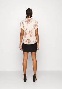 Blusa leggera di colore rosa chiaro con motivo floreale, a maniche corte, abbinata a una gonna nera aderente e scarpe con tacco a blocco. Tessuto morbido, vestibilità comoda.