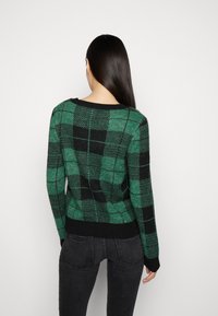 Pull à motifs verts et noirs avec un col rond et des manches longues. Ourlet et poignets côtelés. Présente une texture à carreaux sur toute la surface.