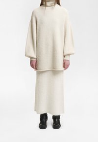 Conjunto de color crema de lana con un top de cuello alto y falda larga. Mangas oversized y textura suave. Botines negros que completan el look.