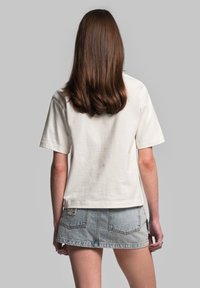 T-shirt in cotone color crema, con maniche corte e una vestibilità comoda. Abbinato a una gonna di jeans, con dettagli di cucitura visibili e tasche posteriori.