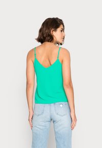 Top verde sem mangas com alças finas ajustáveis, apresentando um decote em V e um corte relaxado, combinado com jeans azul claro.