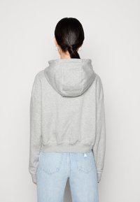 Sudadera gris con una capucha grande, cinturilla elástica y mangas largas, combinada con jeans de tiro alto en azul claro. Vista trasera, con detalles mínimos.