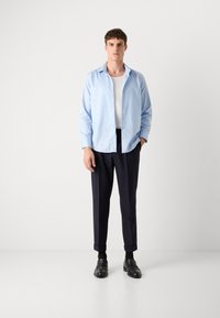 Light blue button-up shirt with a relaxed fit, white undershirt, navy trousers, and black shoes. The shirt has a soft texture and collar.