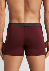 Burgunderfärgade herrboxershorts med svart elastisk midja, slät textur och kroppsnära design, med en medelhög skärning och utan synliga mönster.