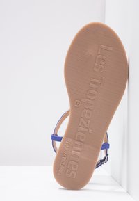 Blå sandal med en platt, strukturerad brun gummisula. Har tunna remmar och ett justerbart spänne. Storlek 37 markerad på sulan.