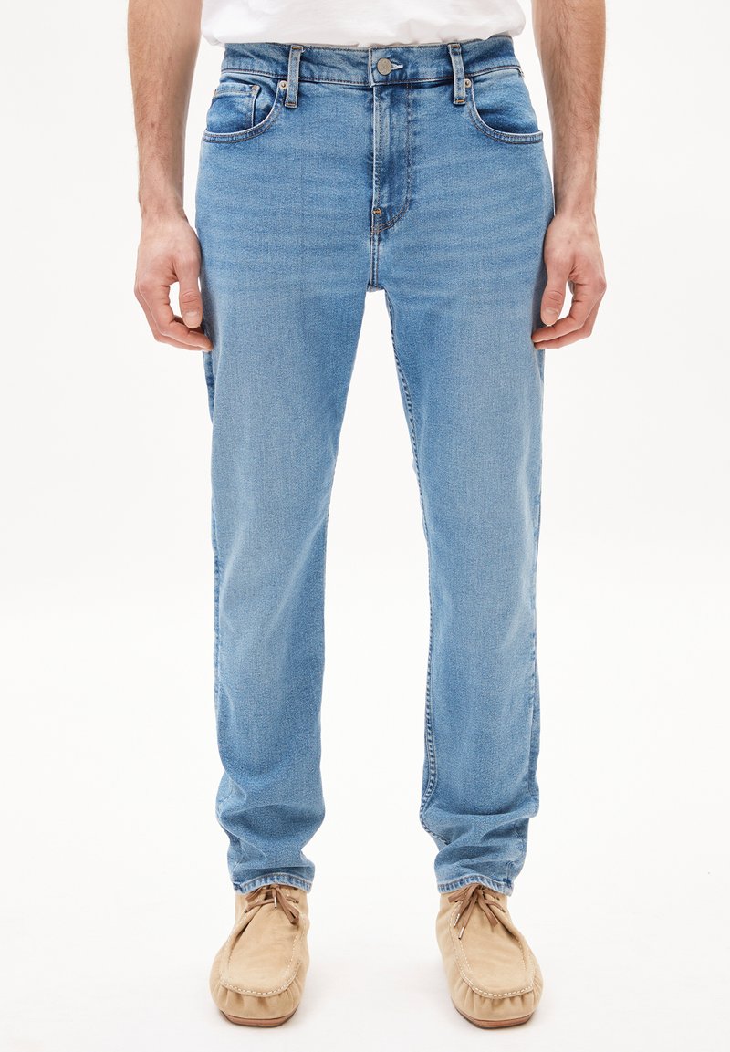 Jean en denim bleu clair avec une coupe droite, cinq poches, passants de ceinture et une légère décoloration. Porté avec des chaussures en cuir moccasin beige.
