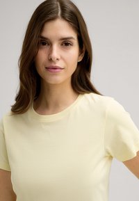 Hellgelbes T-Shirt mit kurzen Ärmeln, Rundhalsausschnitt und dezentem Logo "JOOP!" in der Mitte eingeprägt. Glatter, weicher Stoff.