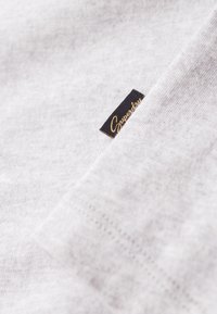 Szara bawełniana tkanina o teksturowanym wykończeniu, z małą czarną metką, na której widnieje złote napisy "Superdry".